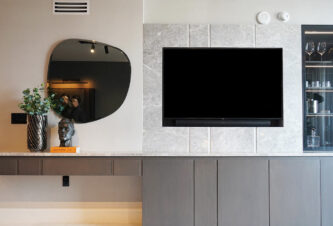 Un apartamento de Brickell con un diseño de pared de TV personalizado que incluye un espejo, una planta, una escultura de sobremesa y un bar.