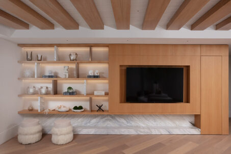 A living room with a built-in TV wall with shelving and wood ceiling beams in a modern luxury penthouse.