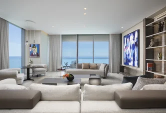 Luxury Miami living room with ocean views, cream sofas, built-in shelving, colorful artwork, and modern coastal interior design