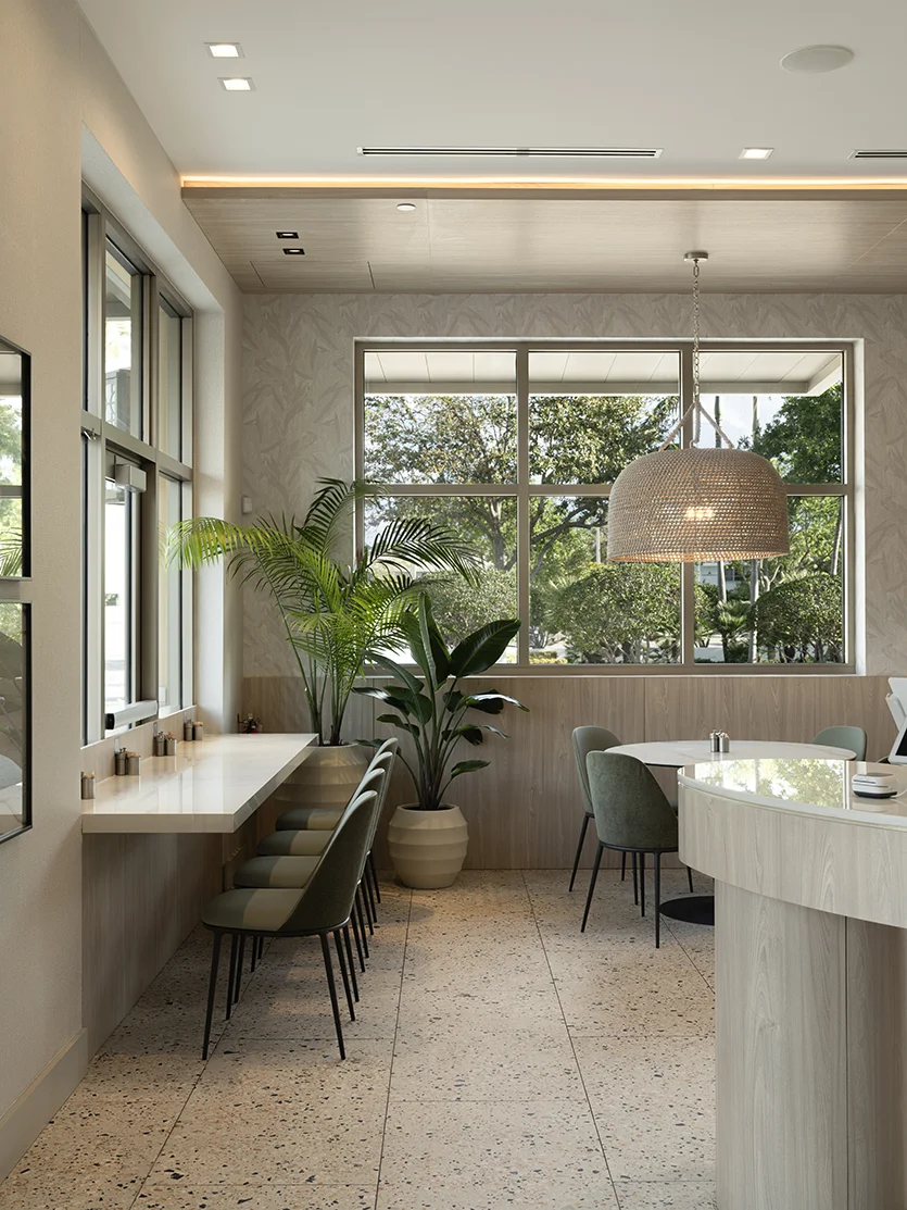 Light-filled restaurant dining area with window counter seating, sage green chairs, woven pendant lighting, indoor plants, and terrazzo flooring