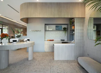 Modern restaurant entry and pickup area with curved light wood counters, open shelving, textured tile, and built-in seating