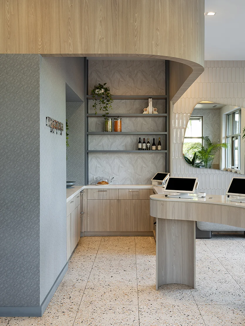 Contemporary restaurant service desk with a curved light wood counter, point-of-sale stations, open shelving, and an arched wall mirror