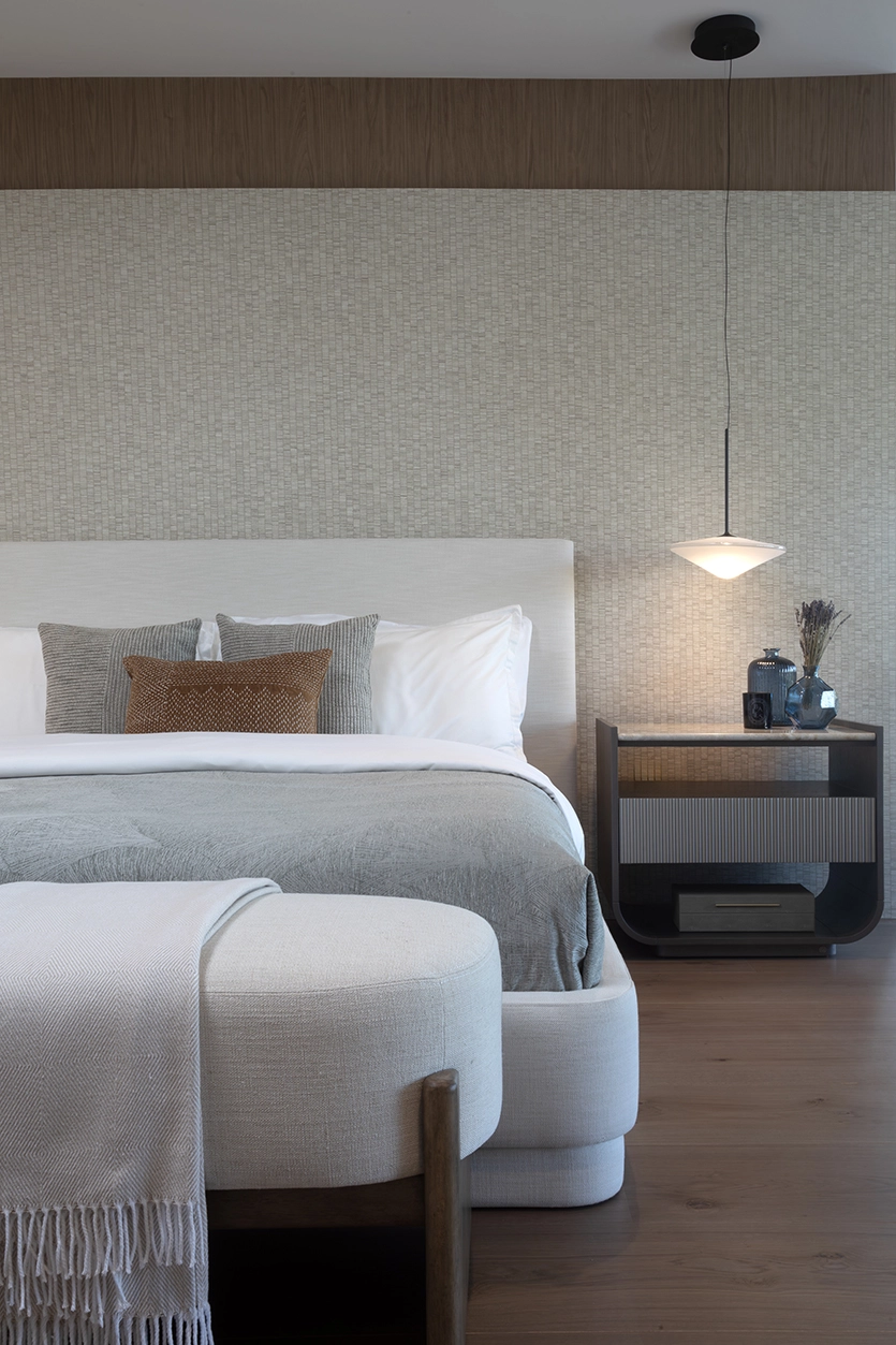 Serene primary bedroom with textured wallpaper, neutral upholstered bed, and modern pendant light in a Coral Gables home.