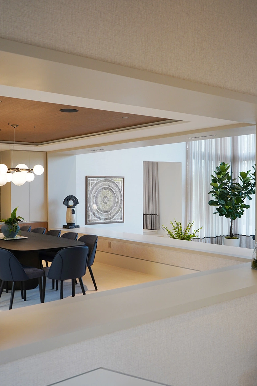 Modern dining room with black chairs and warm wood ceiling opening into a bright living area in Coral Gables.